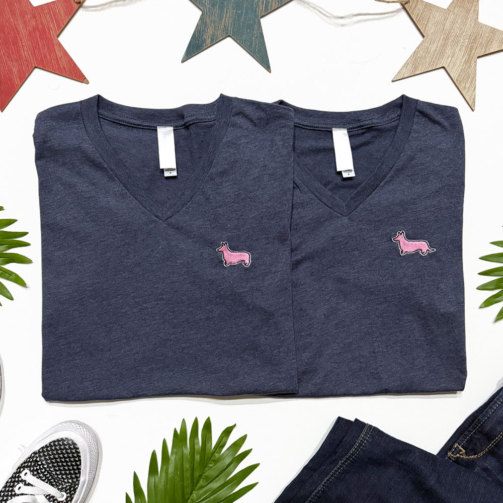 Two folded navy blue V-neck shirts with pink dog illustrations on a white background with decorative elements.